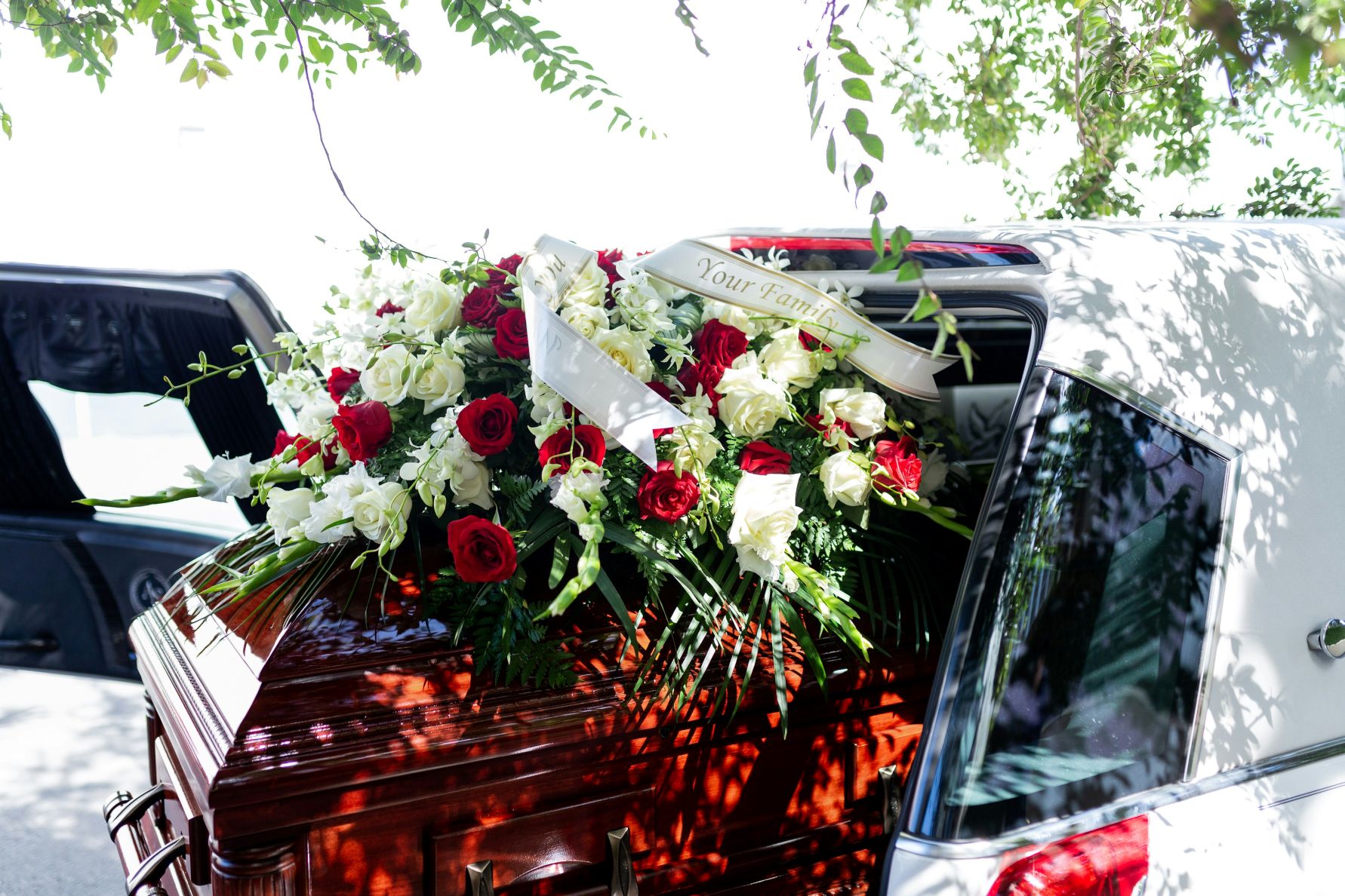 Large red and white flower arrangement and a sash that reads 'Family' atop a wood casket in a hearst.